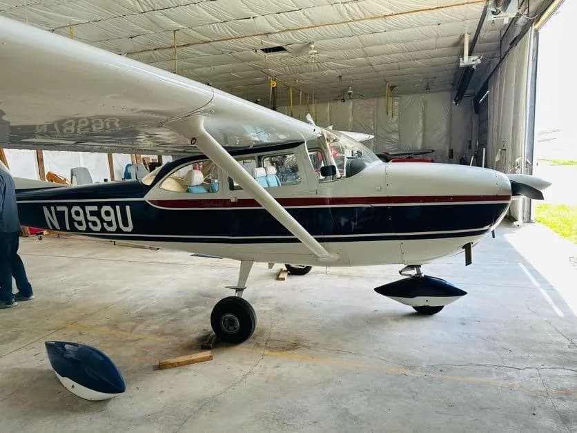 A side view of the white and blue Cessna N7959U with a red stripe parked in a hangar.