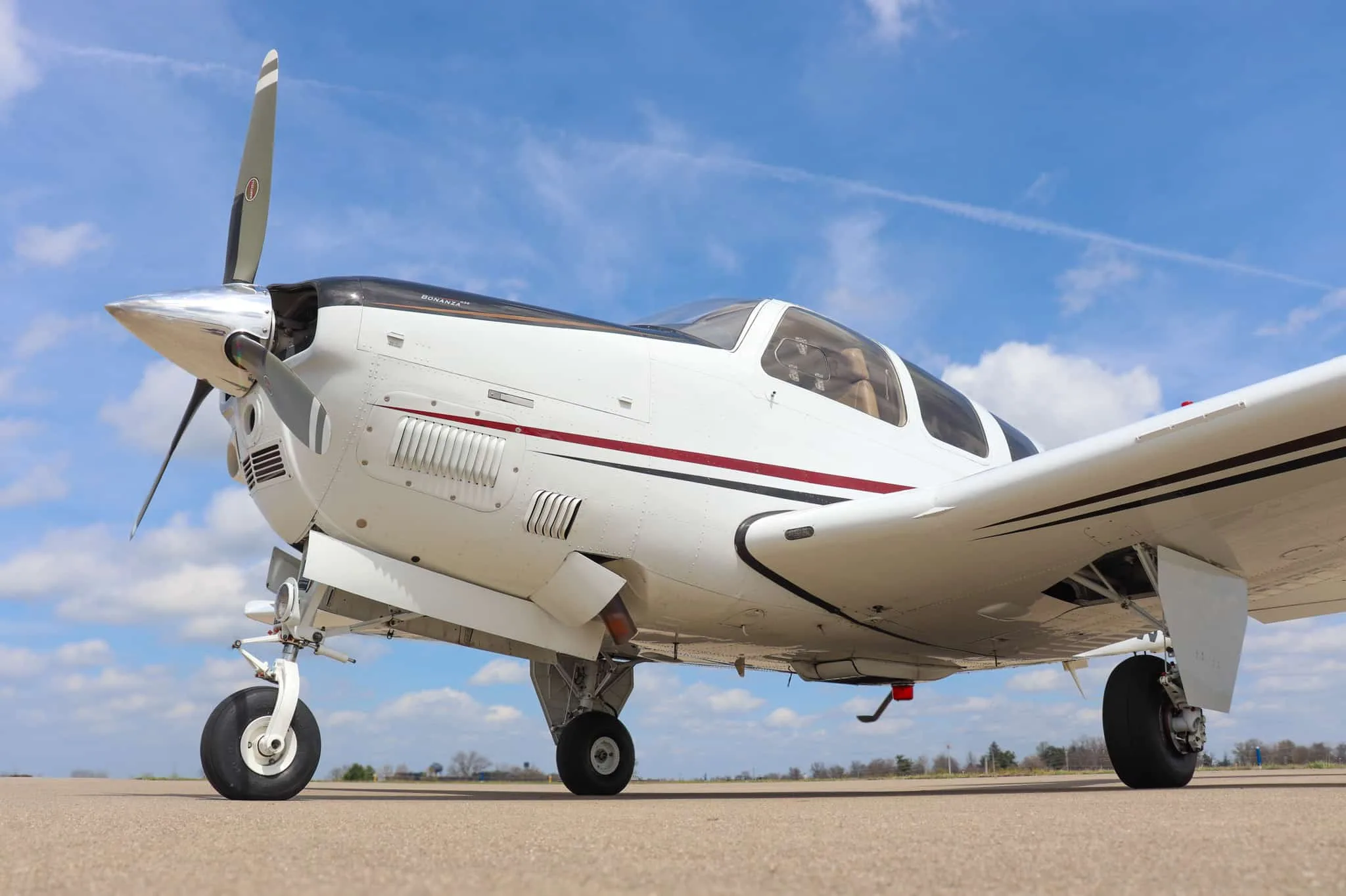 A low-angle side view of a white Beechcraft Bonanza G36 aircraft with its landing gear extended, parked on an airfield.