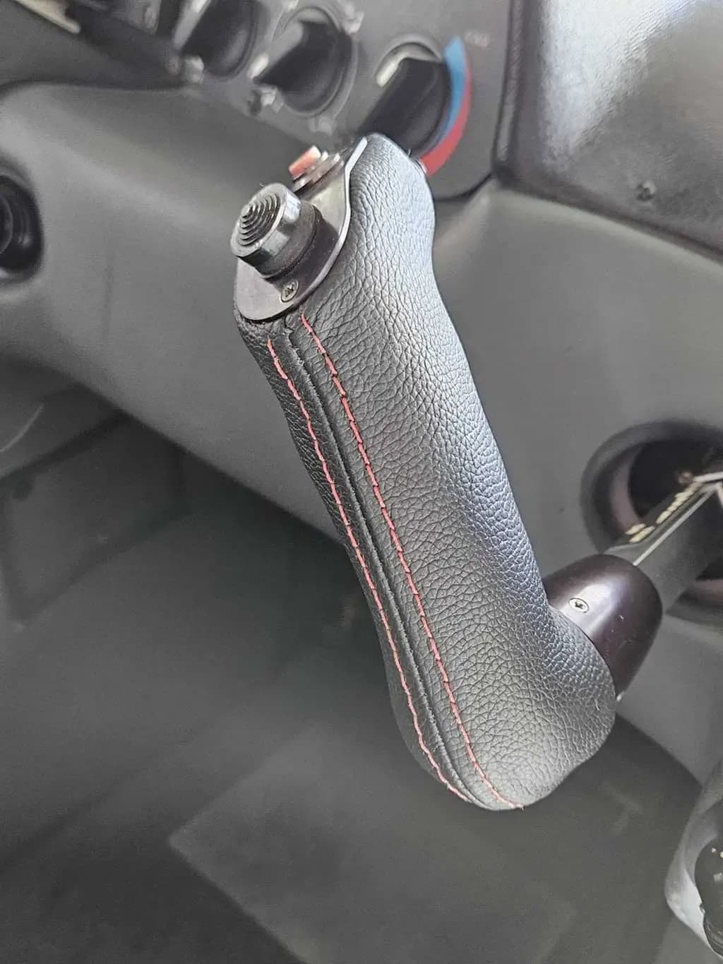 A close-up of an aircraft's black leather-wrapped side stick control with red stitching.