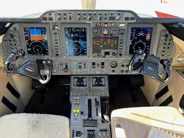 The cockpit of a business jet with a comprehensive instrument panel, multiple digital displays, and control yokes.