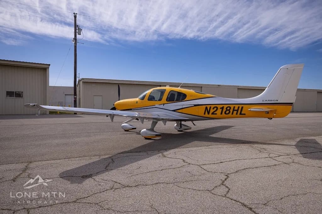 A Cirrus SR22 aircraft with yellow and silver paint scheme parked on an airfield, showing the left side.