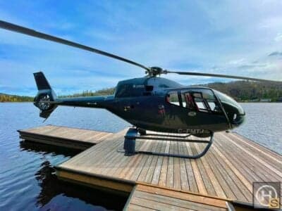 A dark helicopter is parked on a wooden dock by a lake.