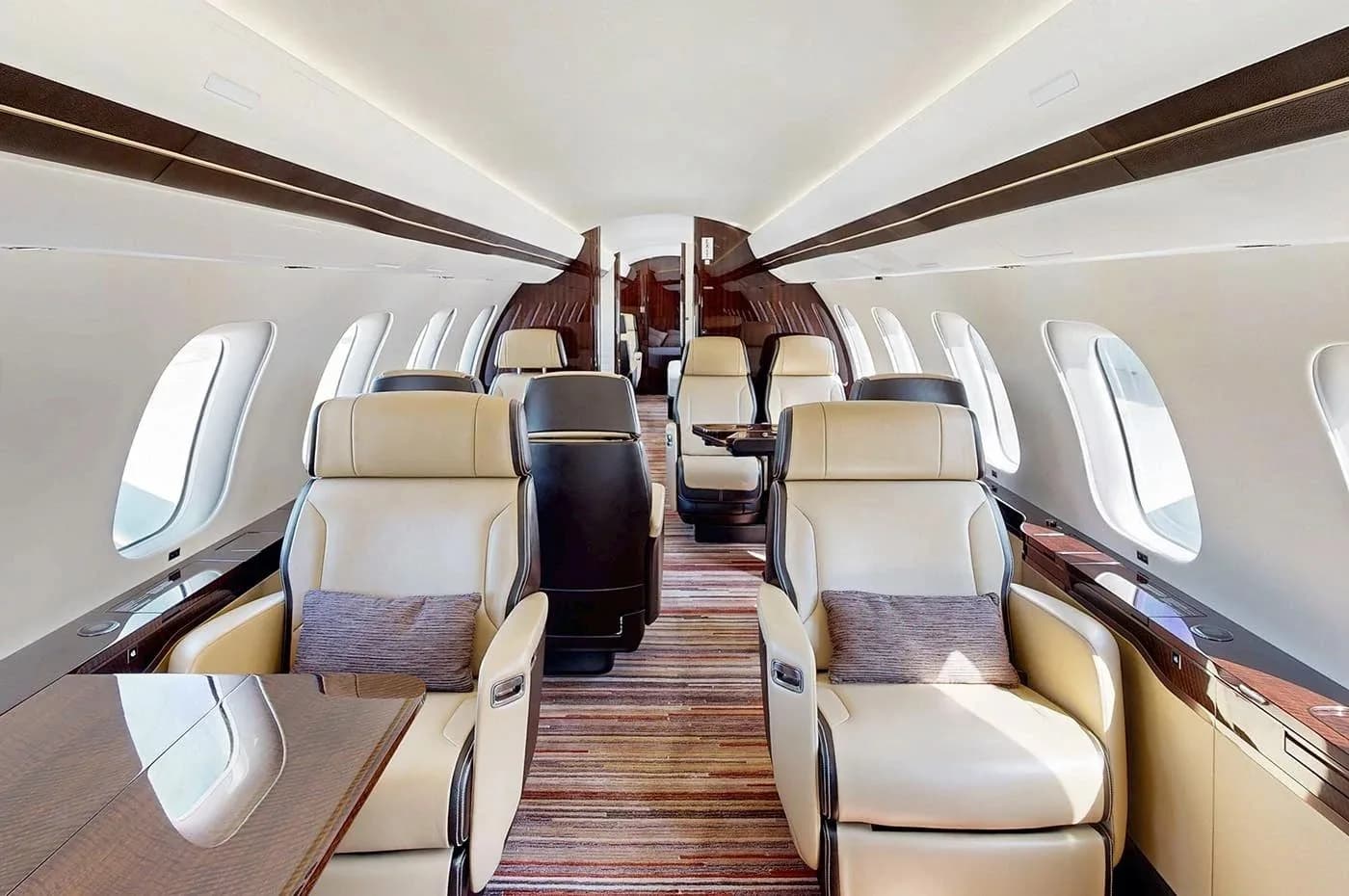 A wider view of the Bombardier Global business jet cabin, showing multiple rows of beige leather seats and a striped carpet.