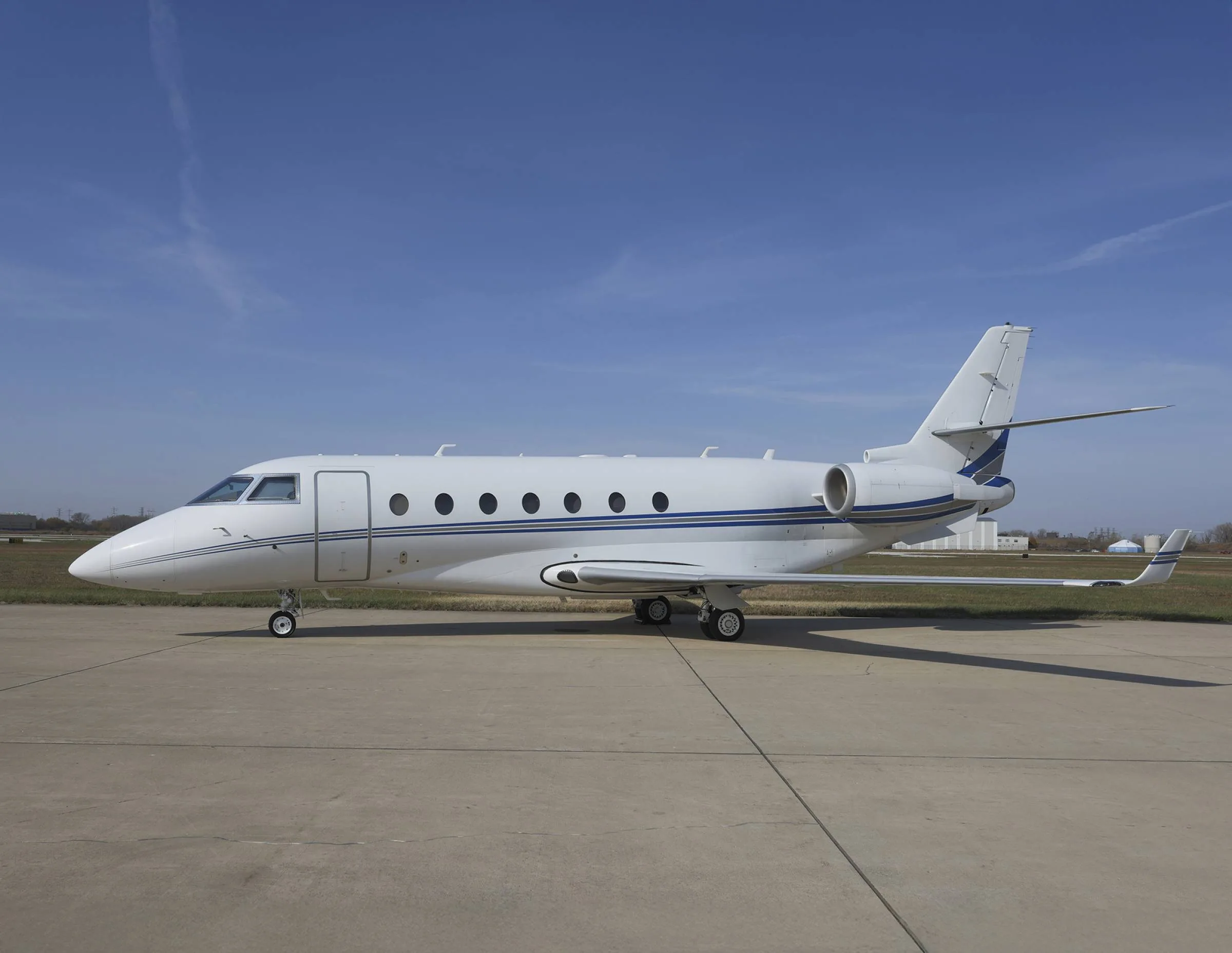 A white and blue Gulfstream jet sits on the tarmac under a blue sky.