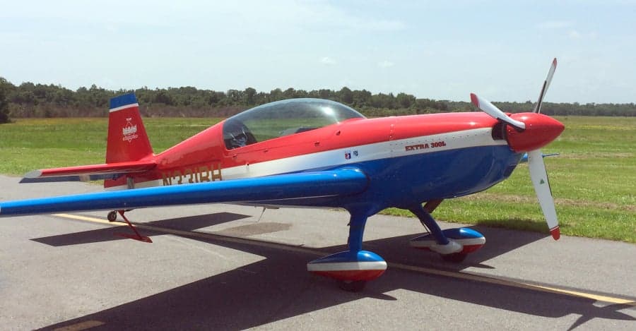An Extra 300L aircraft with a red, white, and blue paint scheme is parked on the tarmac.