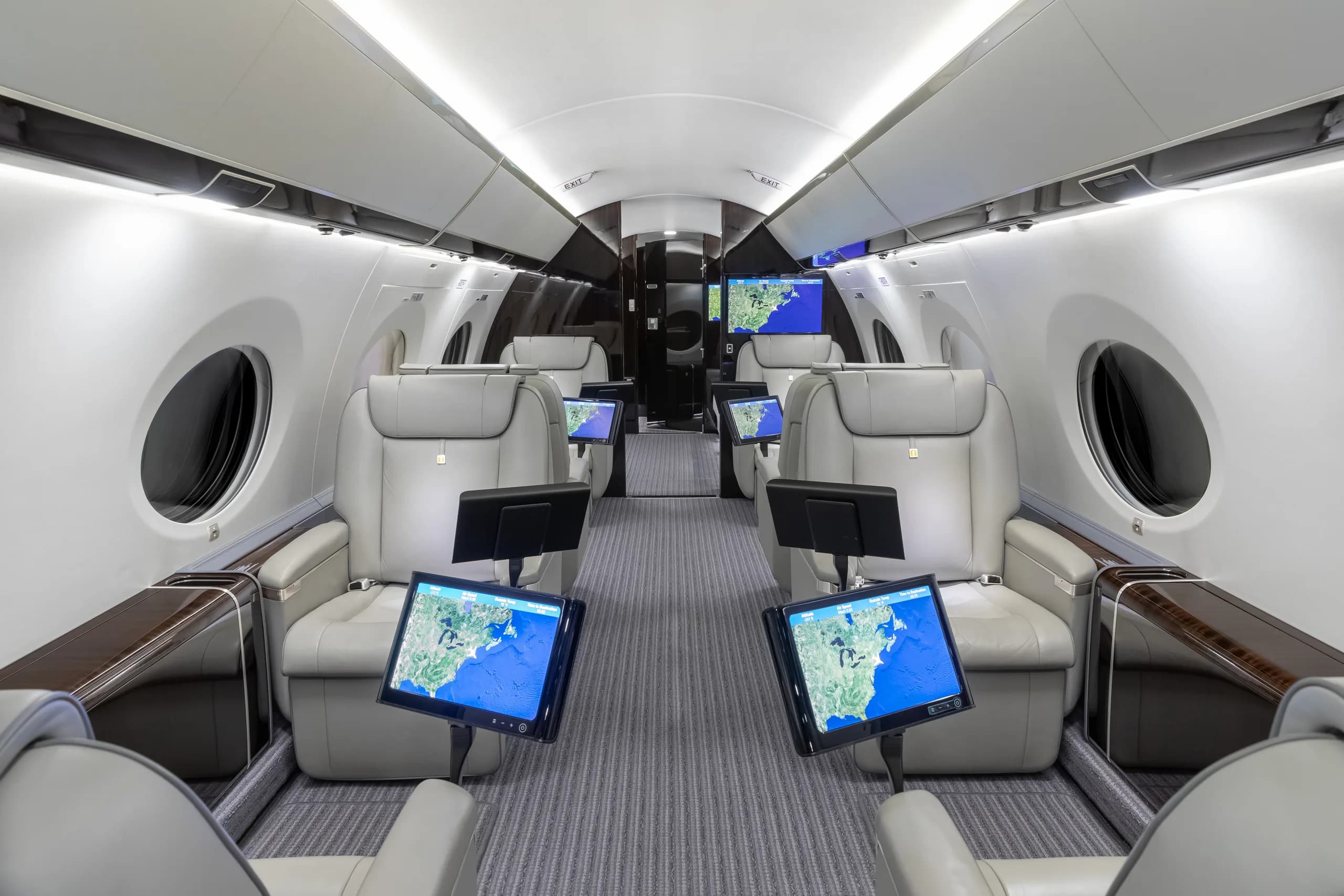 The private jet cabin interior with multiple light grey leather seats, each equipped with a personal screen displaying a map.