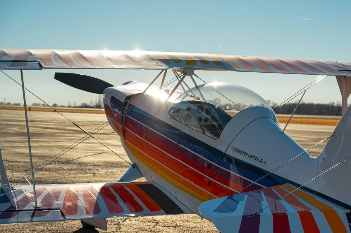Side view of the Christen Eagle II biplane with a colorful paint scheme parked on the tarmac.