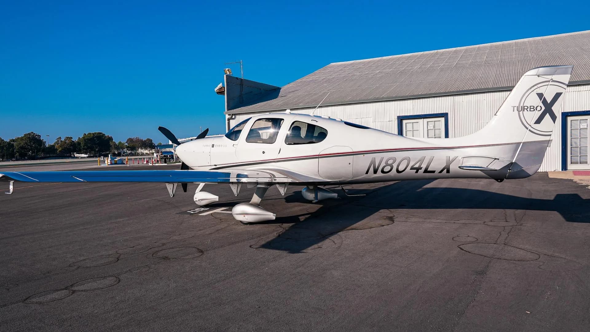 A three-quarter rear view of the white and silver Cirrus SR22T aircraft N804LX parked on an asphalt apron.
