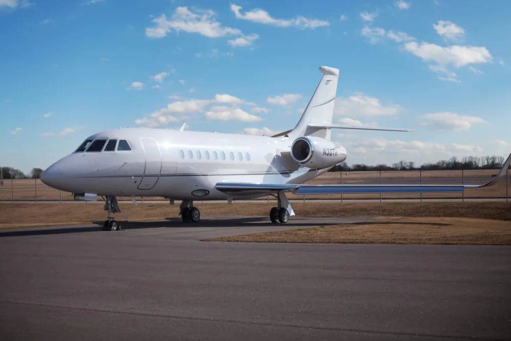 A white Dassault Falcon jet is parked on the tarmac.