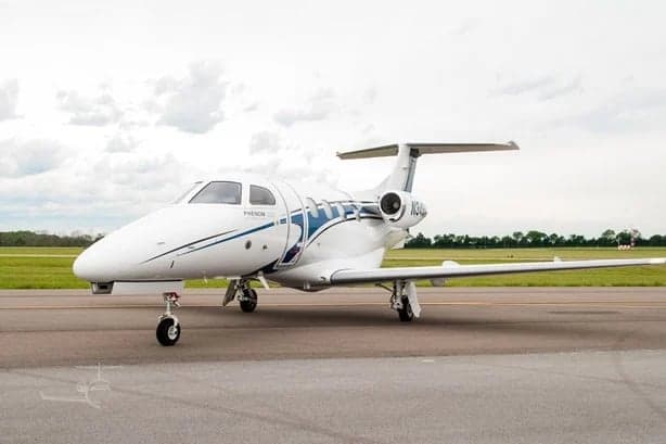 A white Embraer Phenom 300E jet with blue accents, tail number N24Q, parked on a runway.