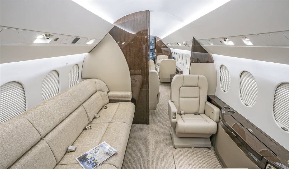 View of the interior cabin of a jet with a couch and leather seats.