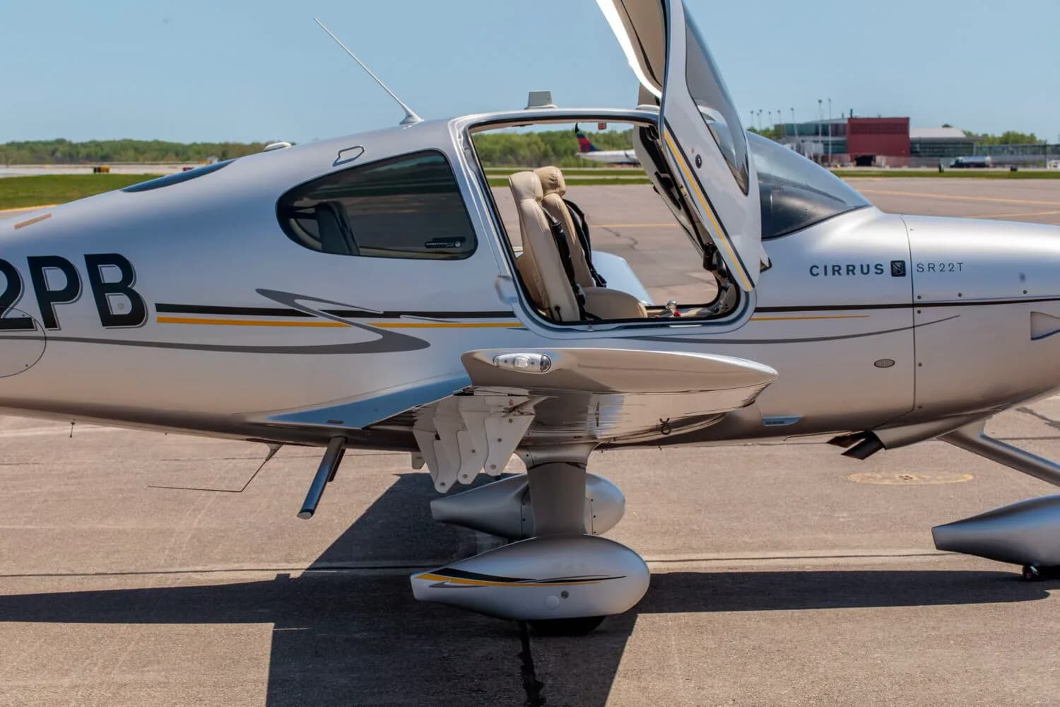 A close-up side view of the silver Cirrus SR22T aircraft, showing the open gull-wing door and part of the interior.
