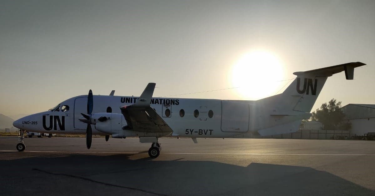 A white United Nations twin-engine turboprop aircraft with registration 5Y-BVT parked on a tarmac at sunset.