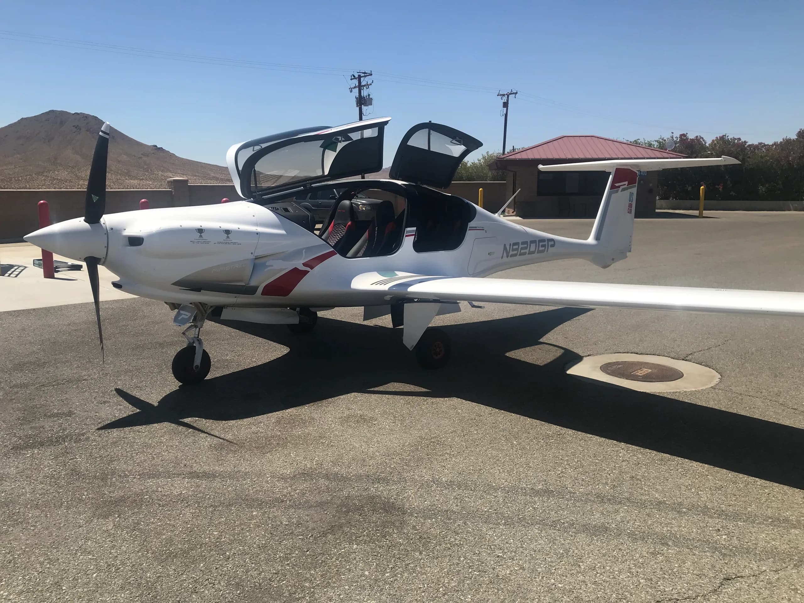 A white Pipistrel Panthera aircraft with red and gray accents, registration N920GP, parked on an airfield with its canopy open.