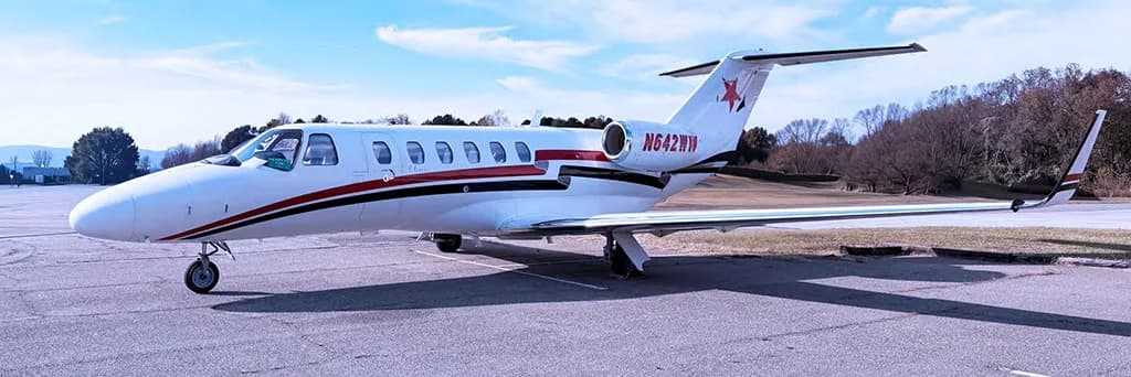 A white Cessna Citation private jet with red and black stripes and tail logo, parked on an asphalt tarmac.