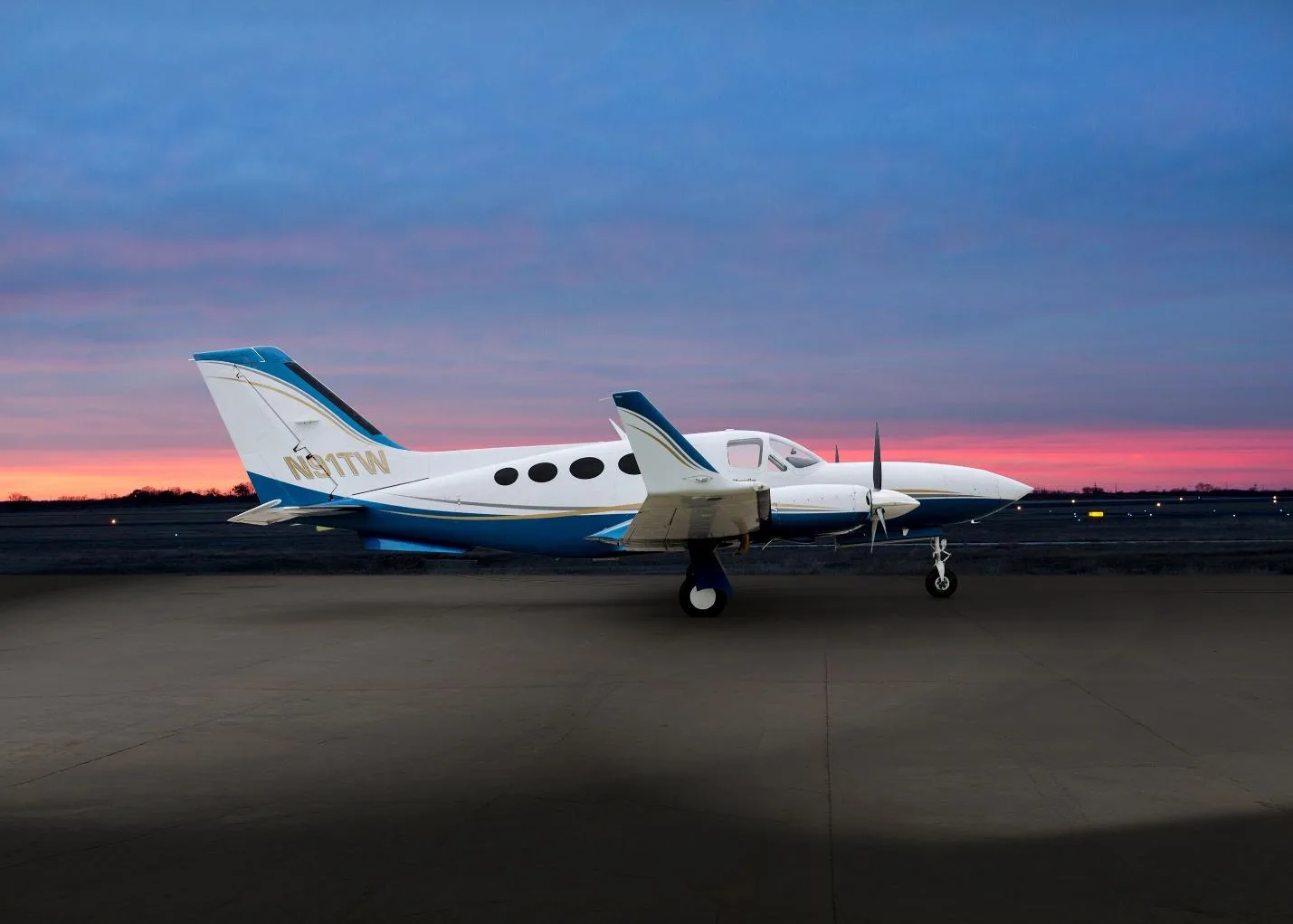 A white and blue Cessna 414 Chancellor (N91TW) parked on an airfield at sunset, viewed from the side.