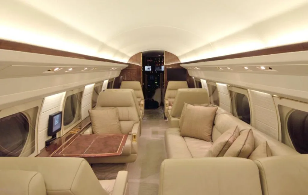 The spacious interior of a private jet with beige leather seating, including a sofa, and wooden accents.