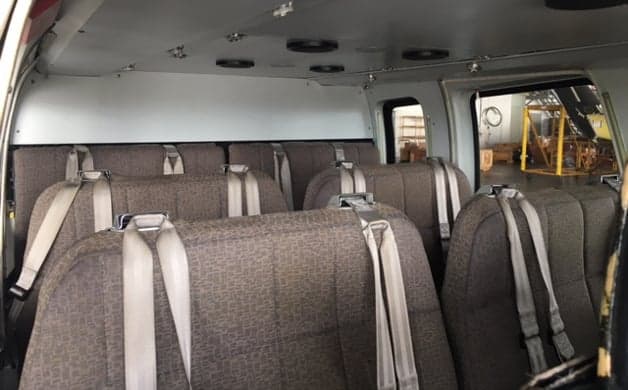 The interior cabin of a helicopter with multiple rows of brown fabric seats and seatbelts.