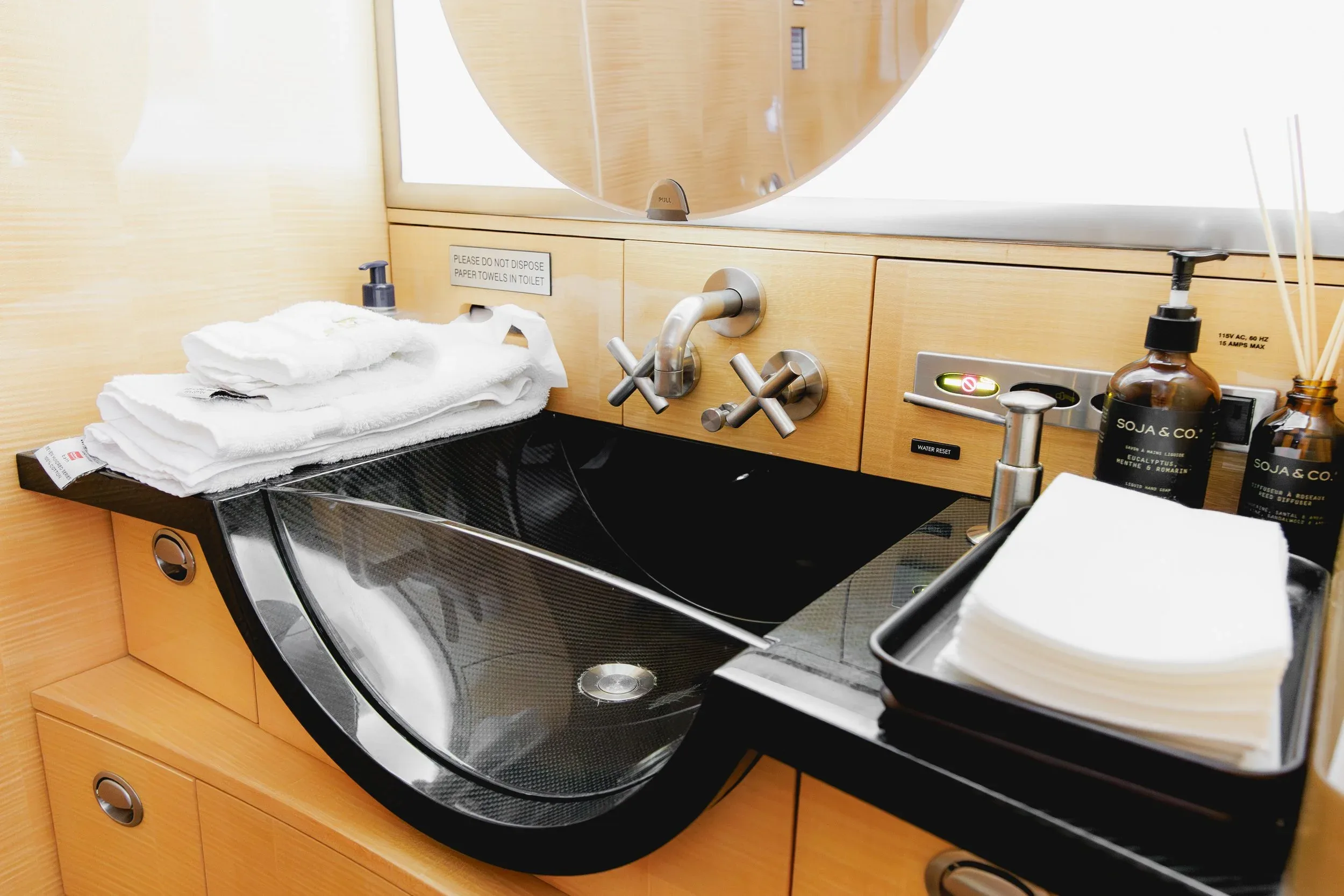 A modern black sink with chrome fixtures and wooden cabinetry in a private jet lavatory, with towels and toiletries.