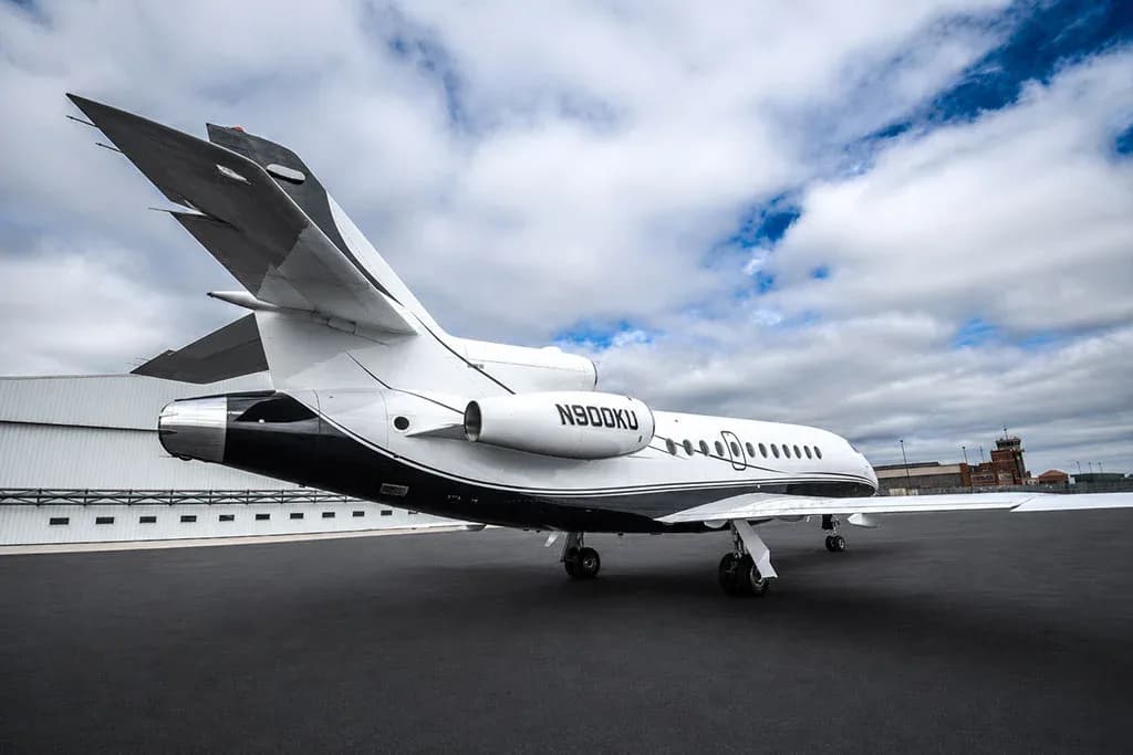 A rear view of the Dassault Falcon 900EX business jet, registration N900KU, parked on a tarmac with a control tower in the distance.
