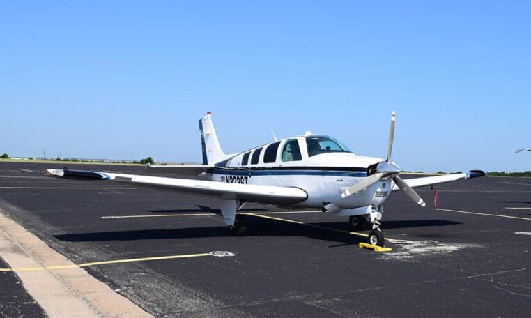 A front-side view of a white and blue Beechcraft Baron aircraft, N3236T, parked on an asphalt tarmac.