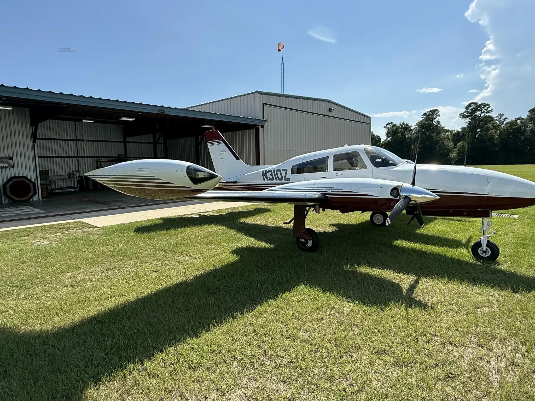 Side-right view of a white and red twin-engine aircraft (N310Z) parked on grass next to a hangar.