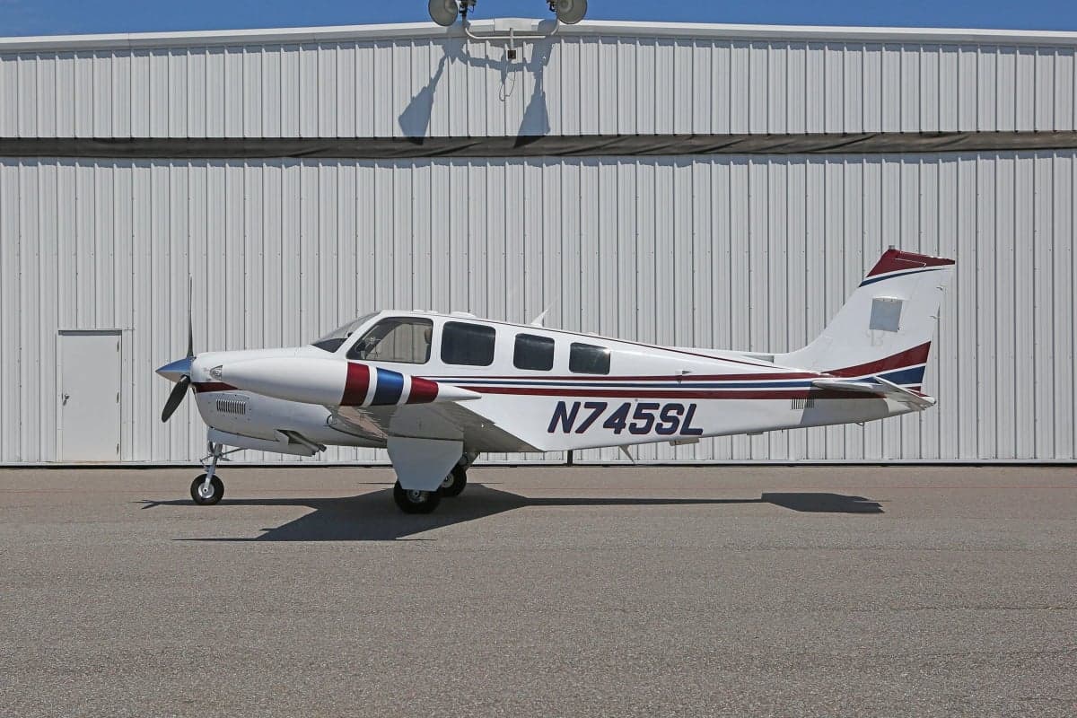 Side view of a white and red Beechcraft Bonanza aircraft with registration N745SL parked in front of a hangar.