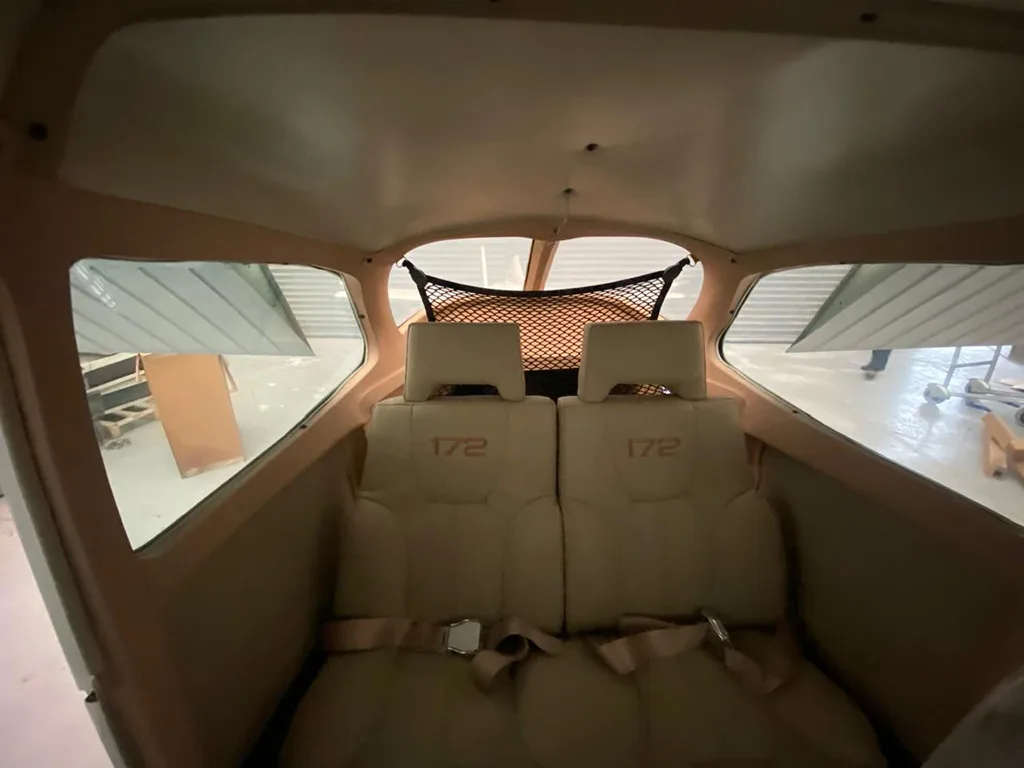 The rear cabin interior of a Cessna 172 aircraft with two tan seats marked "172" and a cargo net.