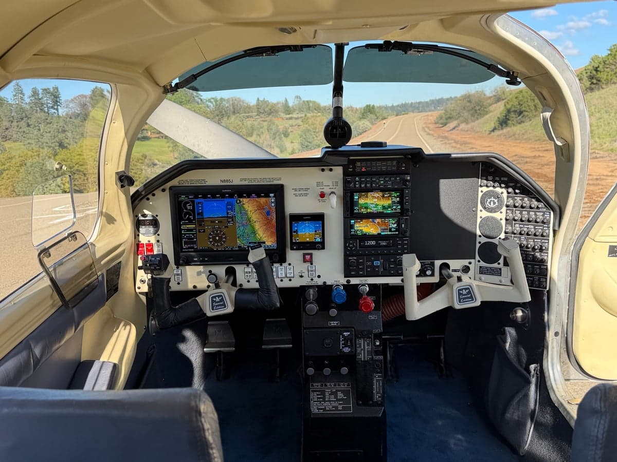 Wide view of the Mooney M20J cockpit from the open doorway, showing the instrument panel and seats.