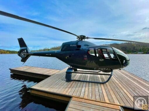 An Airbus helicopter, registration C-FMTJ, is parked on a wooden dock on a lake.