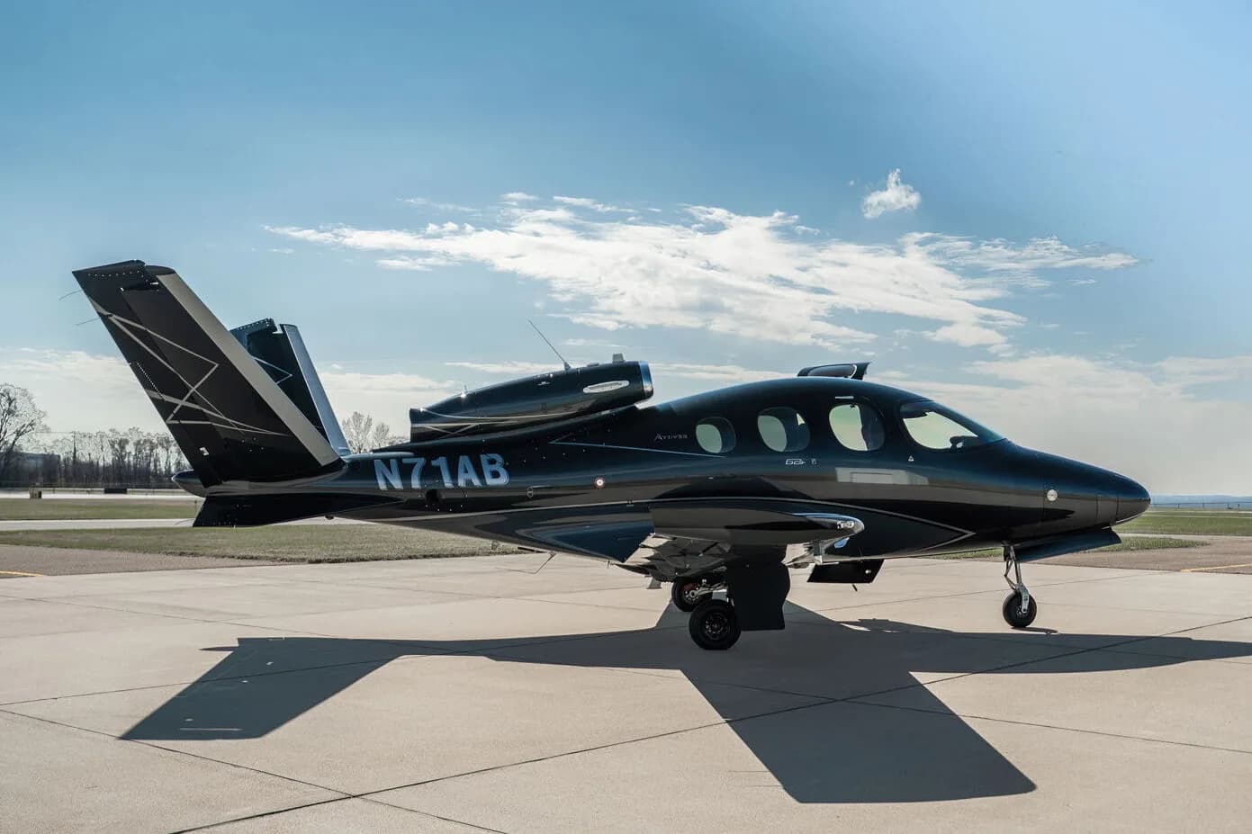 Side view of a black Cirrus Vision Jet (N71AB) with a grey underside and geometric tail design, parked on an airport tarmac.