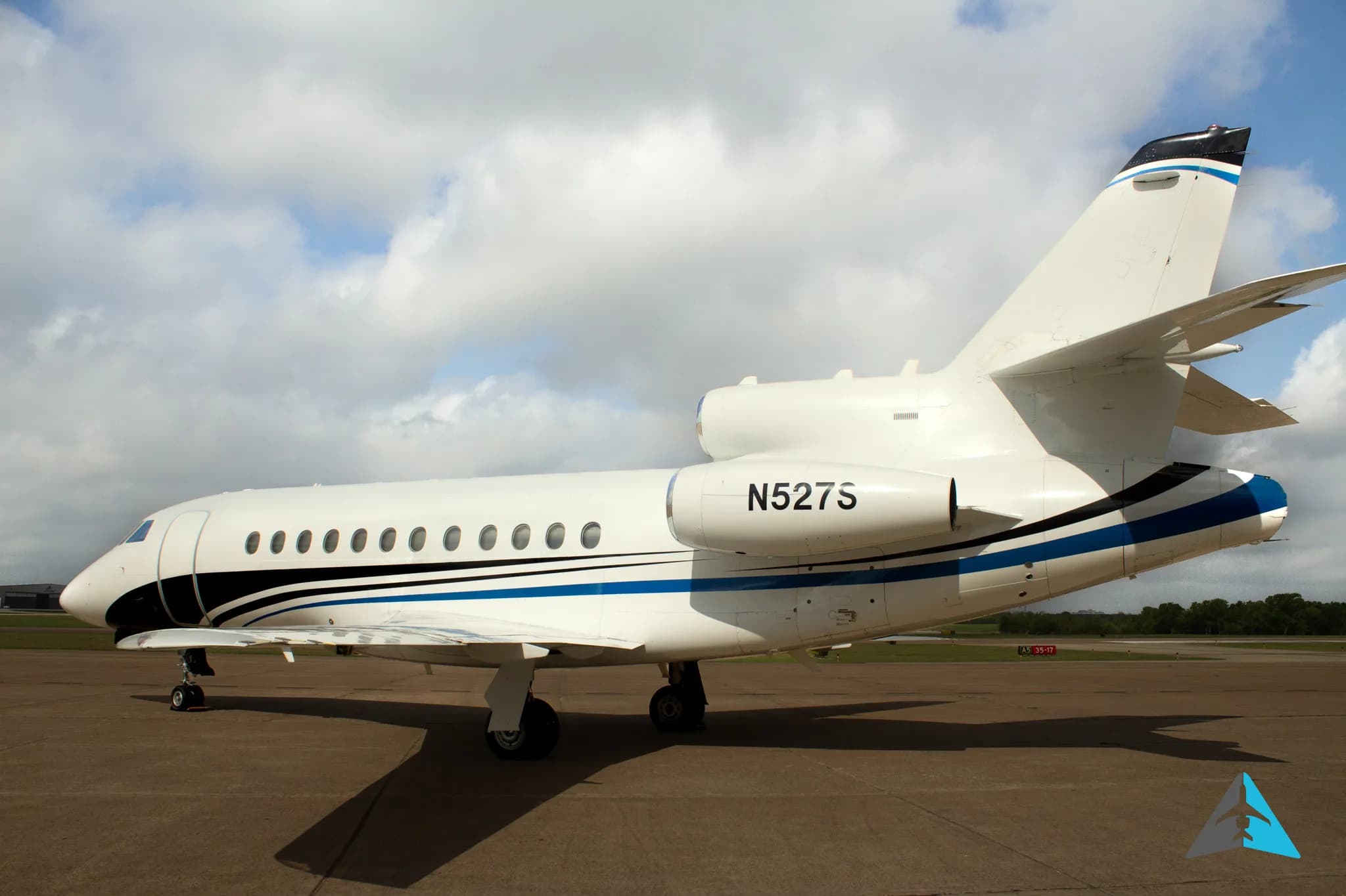 A rear-side view of a white Dassault Falcon 900EX business jet with black and blue stripes, parked on an airfield.