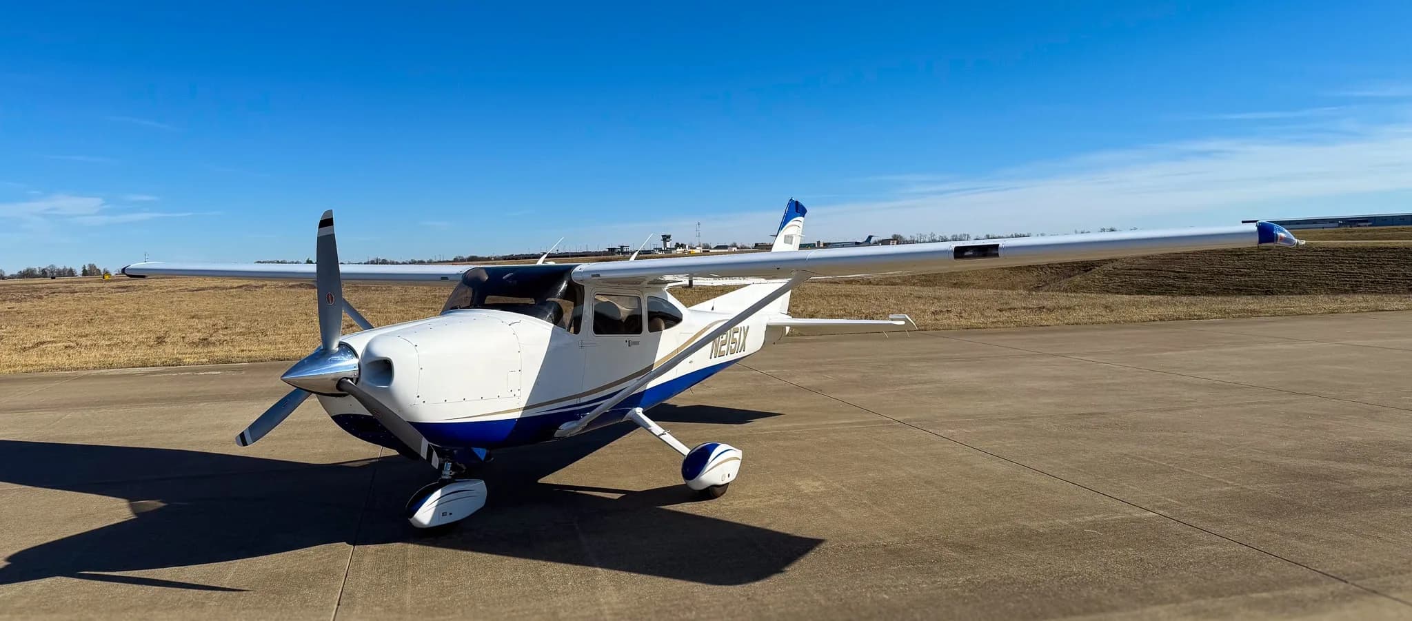 A white and blue Cessna 182 Skylane (N2151X) parked on a tarmac, viewed from the front-left.