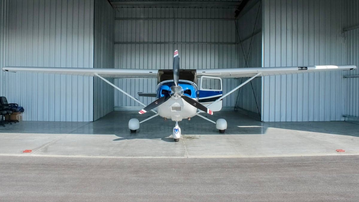 A white and blue single-engine propeller aircraft, N923DM, parked inside a metal hangar, viewed from the front.