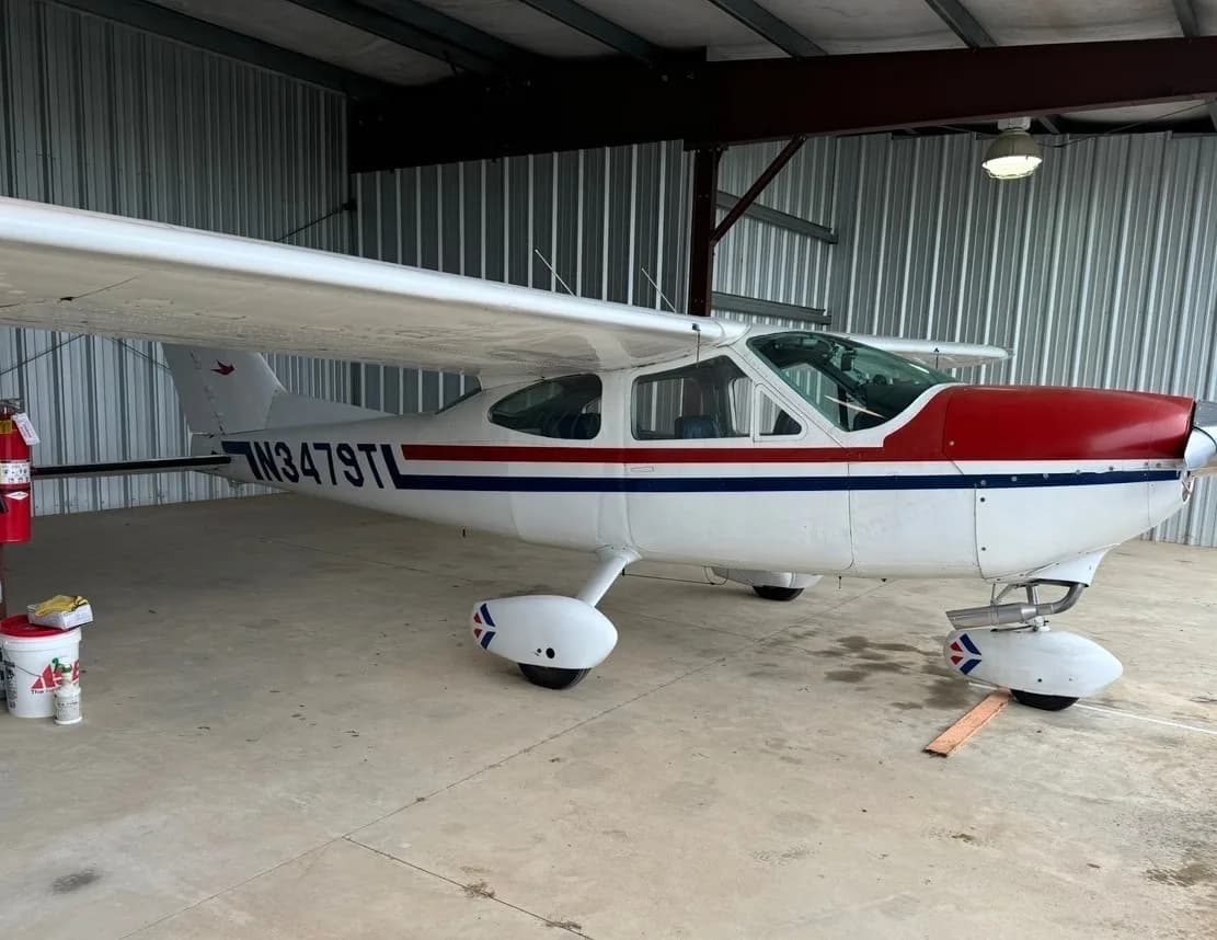 A white Cessna 182 with red and blue stripes, registration N3479T, parked inside a hangar.
