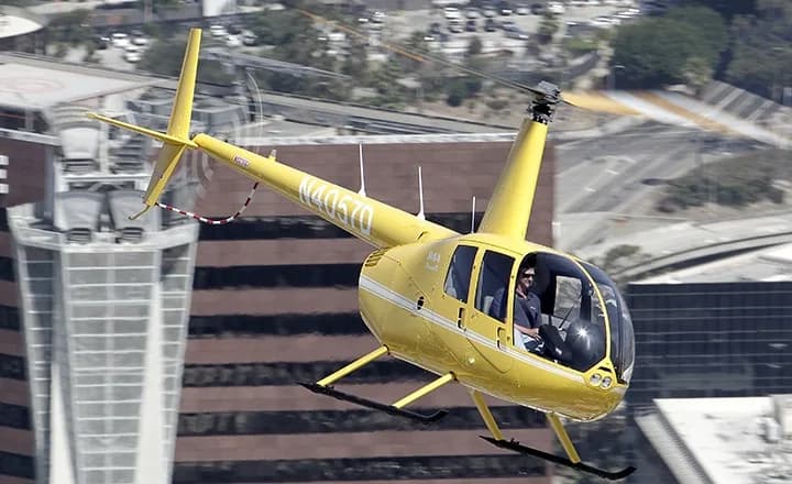 Yellow Robinson R44 helicopter flying over a city.