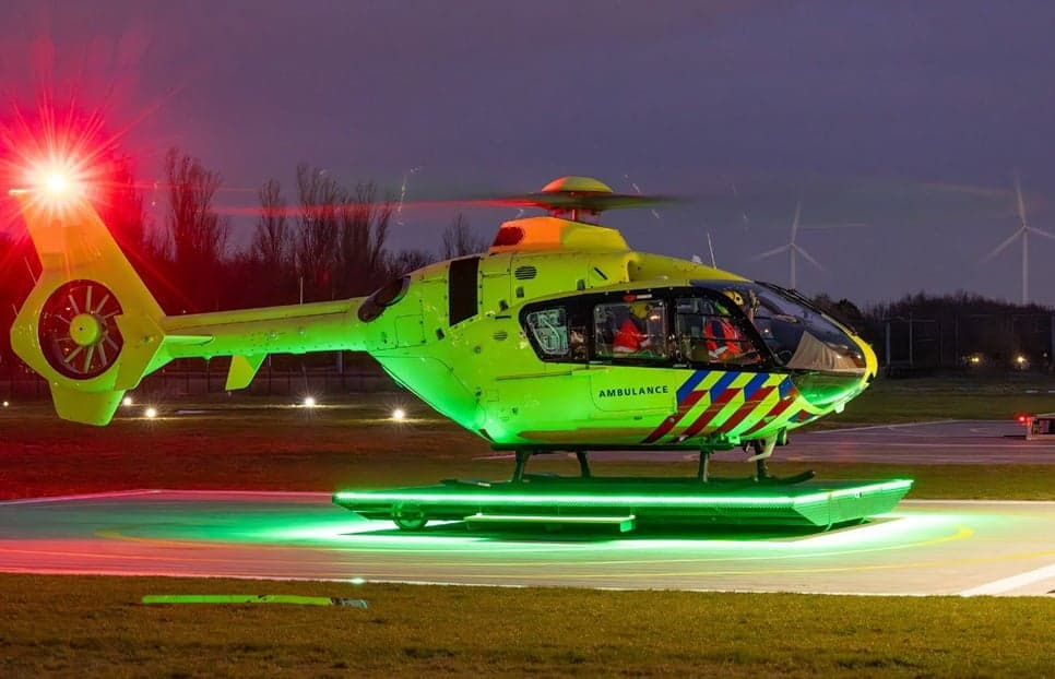 A bright green ambulance helicopter with red and blue stripes is illuminated on a helipad at night.