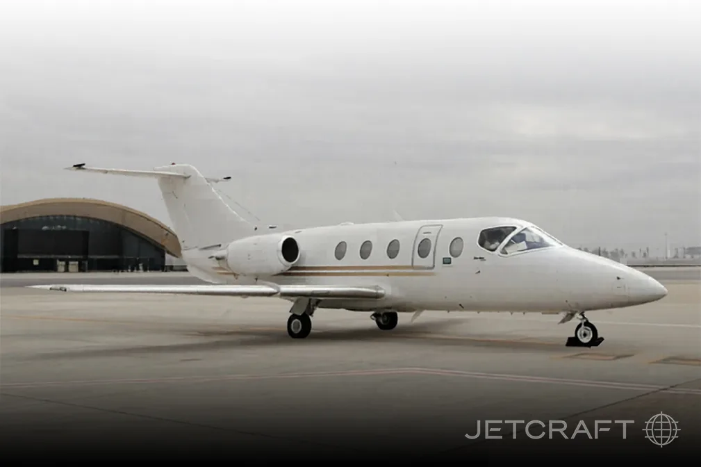 A white business jet with gold stripes on the tarmac in front of a hangar.
