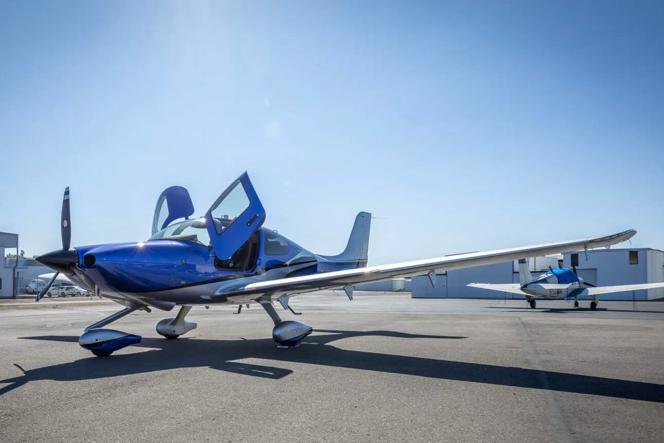 A three-quarter front view of the blue and silver Cirrus SR22 aircraft, N275MG, with its doors open on the tarmac.