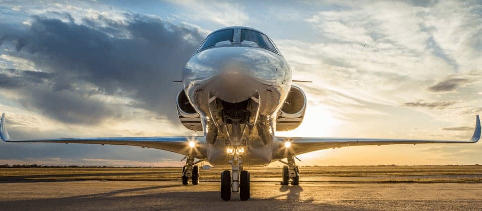 A private jet parked on the tarmac at sunset.