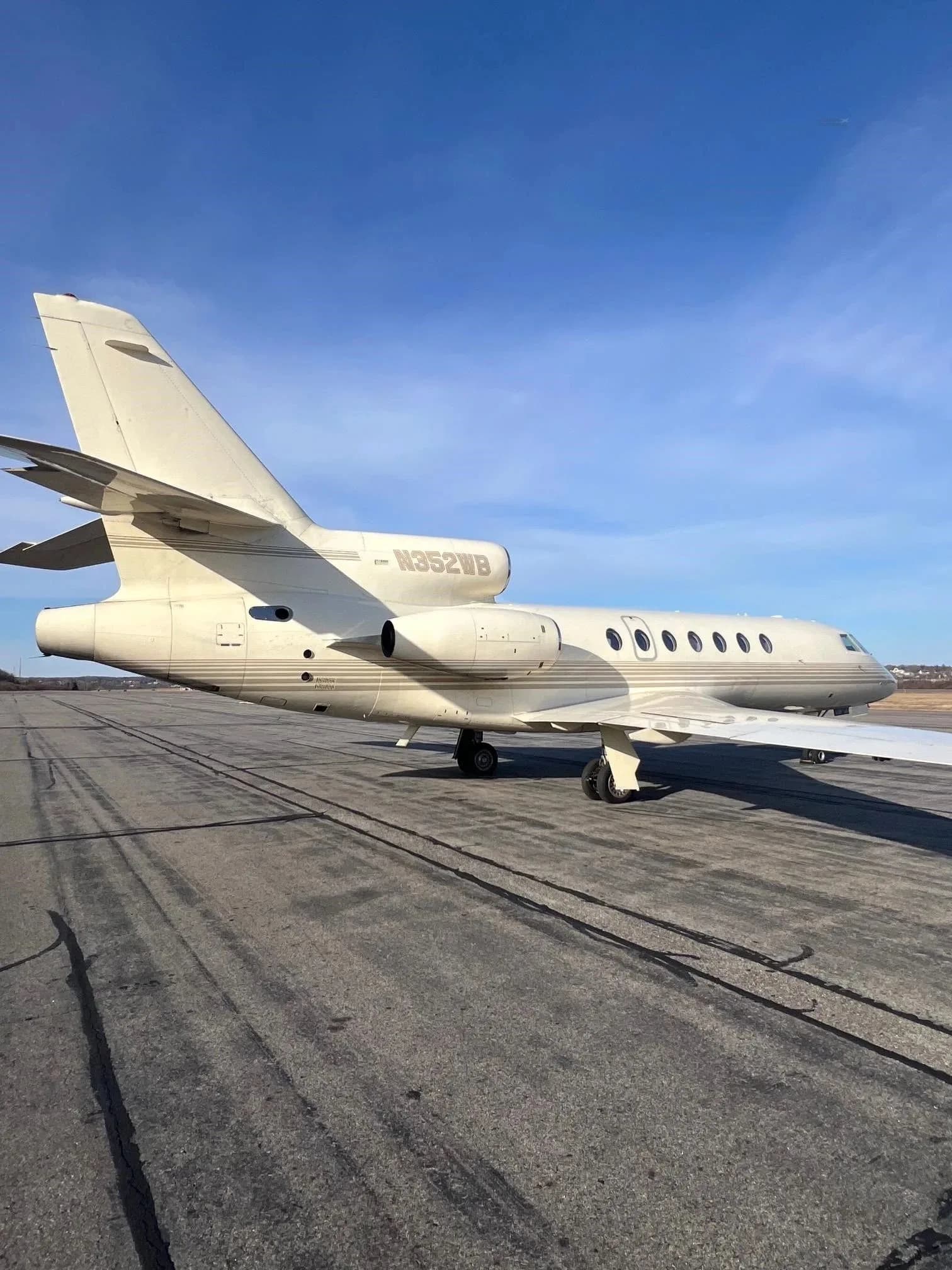 A rear-side view of a beige Dassault Falcon 900EX business jet with N352WB registration on the tail, parked on an airport tarmac.