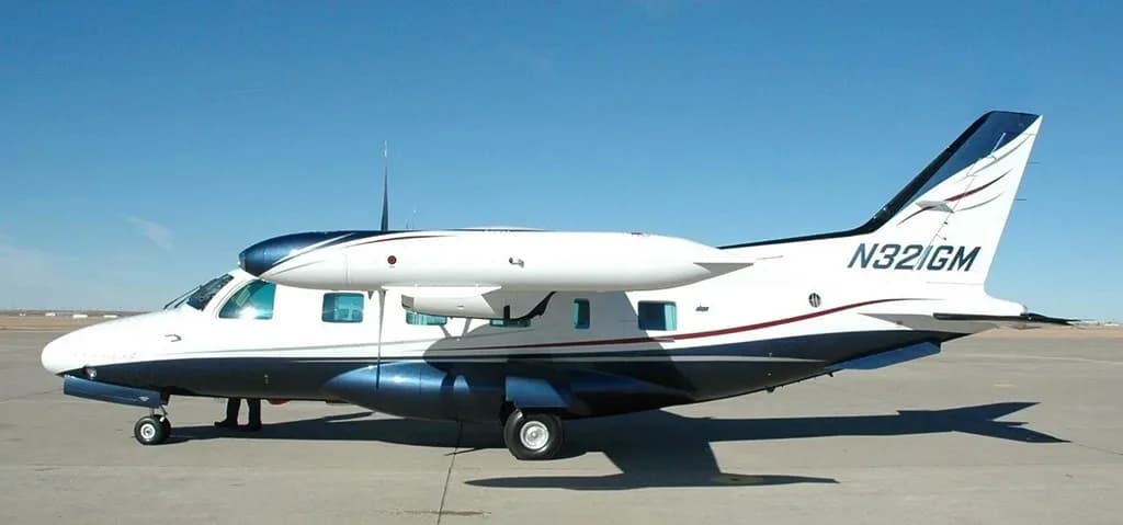 A side view of a white and blue twin-engine turboprop aircraft, registration N321GM, parked on an airfield.
