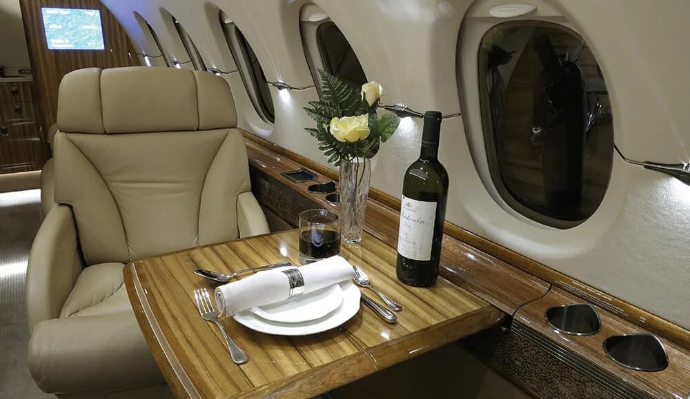 A close-up of a set dining table with a bottle of wine and flowers inside the aircraft cabin.