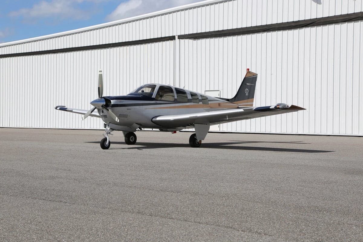 A Beechcraft Bonanza aircraft parked on the tarmac in front of a hangar.