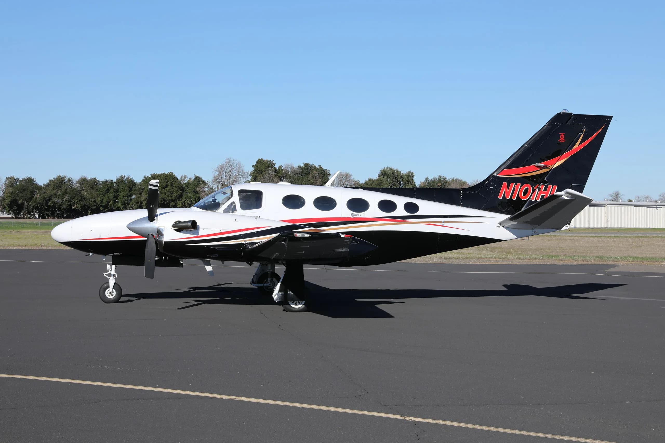 A side view of the white, black, and red Cessna 414 Chancellor parked on an asphalt tarmac.