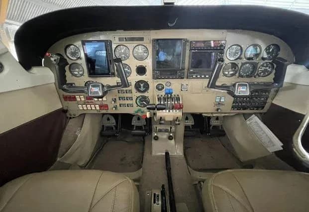 The cockpit of a small aircraft, showing the instrument panel with analog gauges and digital displays, and dual yokes.