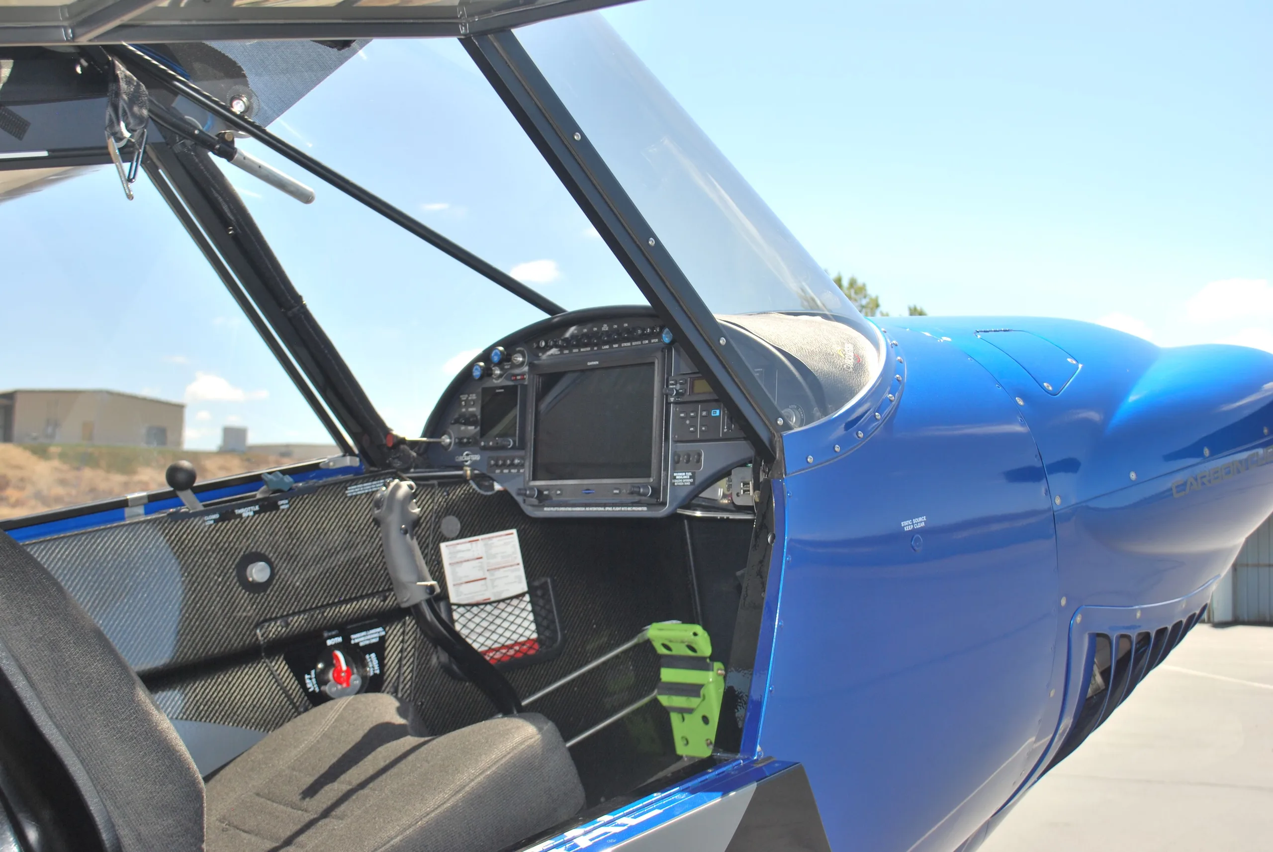 A view into the cockpit of a blue Carbon Cub FX3, showing the instrument panel with a large display and carbon fiber interior.