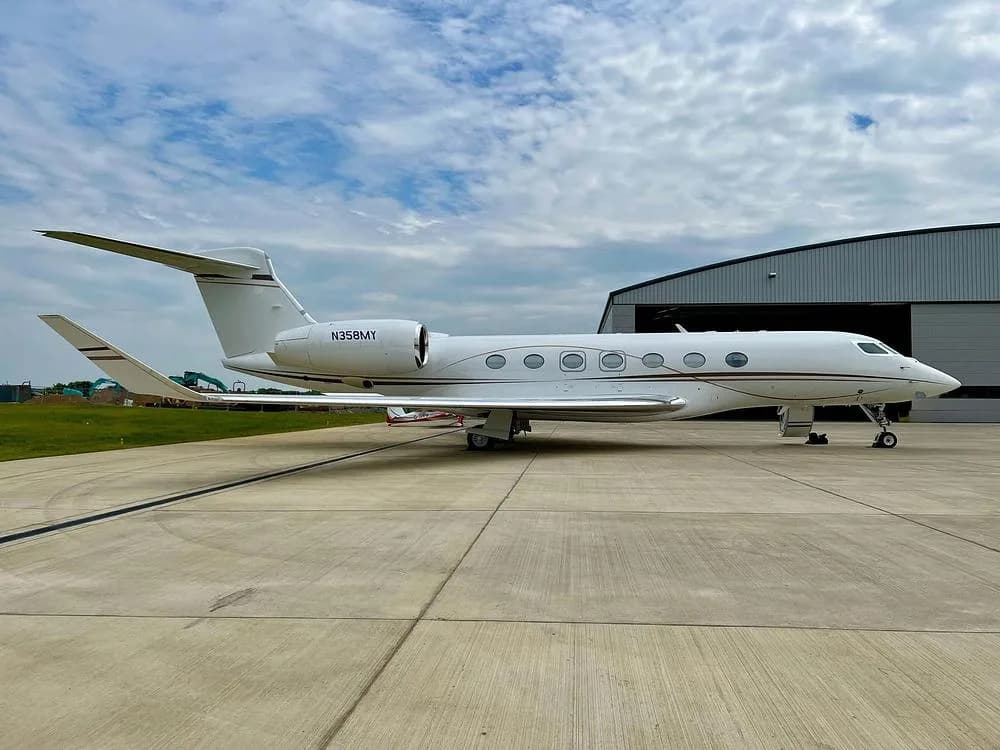 A white Gulfstream G650 business jet with tail number N358MY parked on a tarmac next to a hangar.