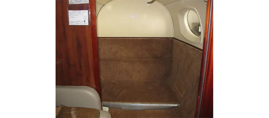 Rear interior of the aircraft with carpeted wall and small window.