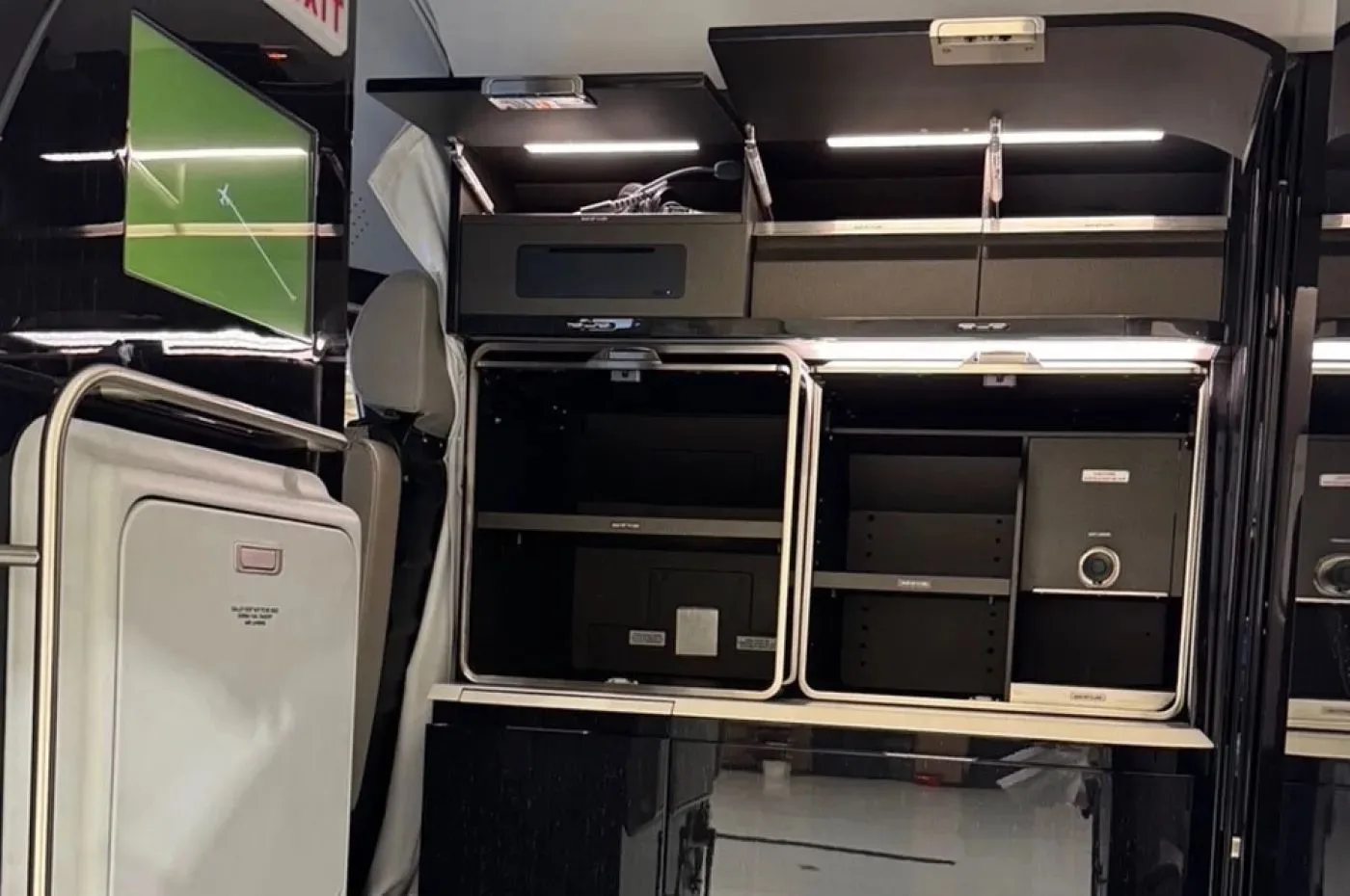 An open galley or entertainment console in an aircraft interior, revealing multiple compartments and a small screen.